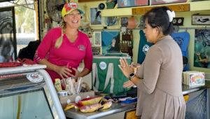 A woman stands and smiles behind a county at Aripeka Stone Crab Compnay, helping a customer check out. 